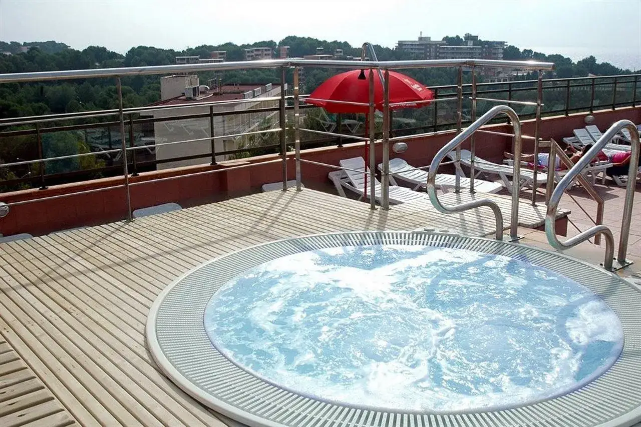 Jacuzzi burbujeante en la terraza del hotel htop molinos park, con tumbonas y sombrilla roja al fondo.