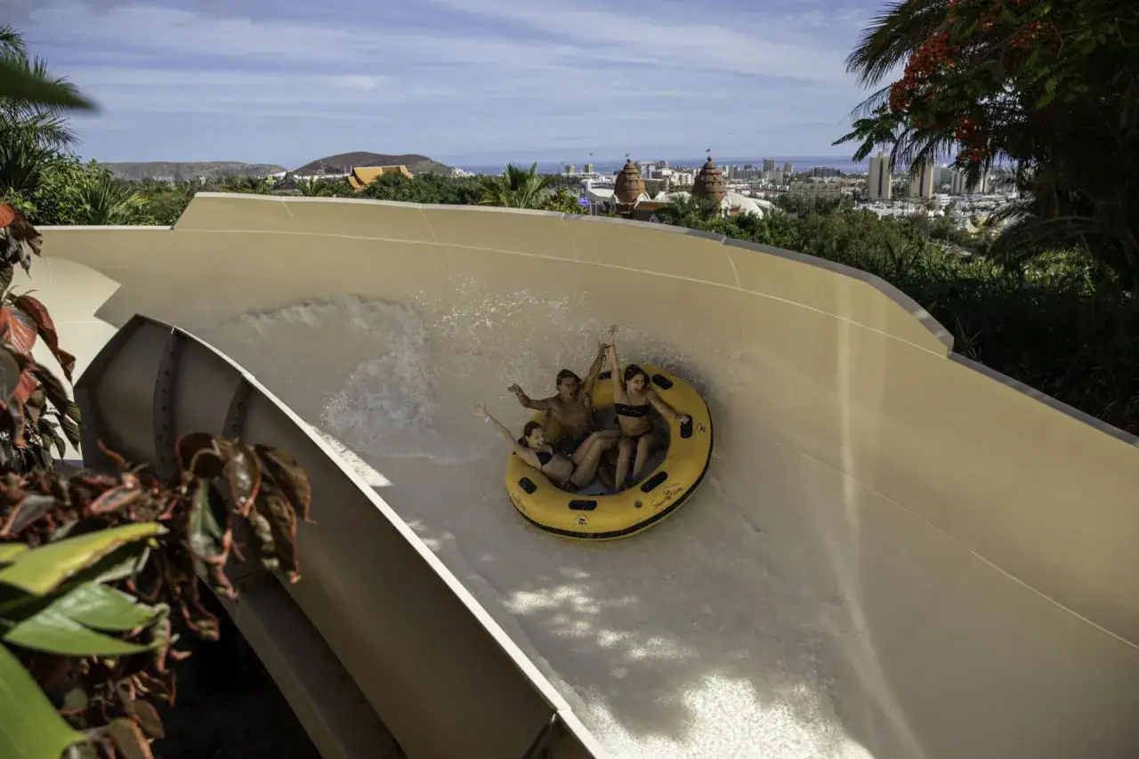 Diversión acuática en Tenerife con niños: familia en un flotador amarillo desciende por un tobogán.