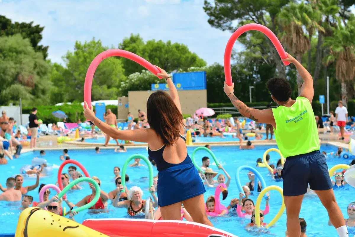 Animadores dirigen una clase de aquagym en la piscina del Club Mac Alcudia. Niños y adultos disfrutan con flotadores de colores.