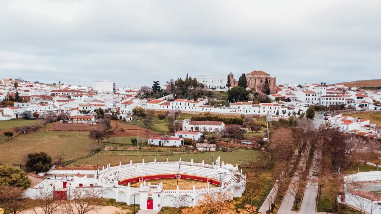 Vista panorámica de Cazalla de la Sierra, con su plaza de toros blanca y roja en primer plano y el pueblo blanco escalonado en la colina.