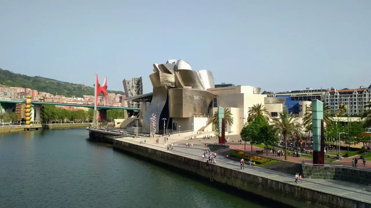 Museo Guggenheim y el puente rojo, un buen plan para ver en Bilbao en 1 día. Paseo junto a la ría con gente disfrutando del sol.