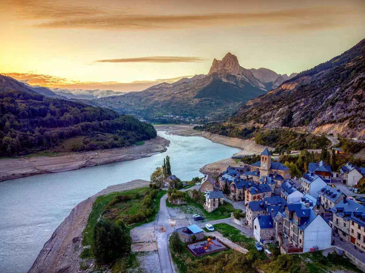 Pueblo de piedra junto a un embalse, con montañas imponentes al fondo. Un ejemplo de los pueblos más bonitos de Huesca.