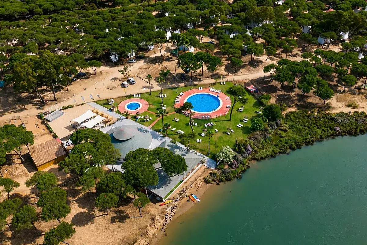 Vista aérea del hotel Occidental Isla Cristina, con piscinas, césped, pinos y un río.