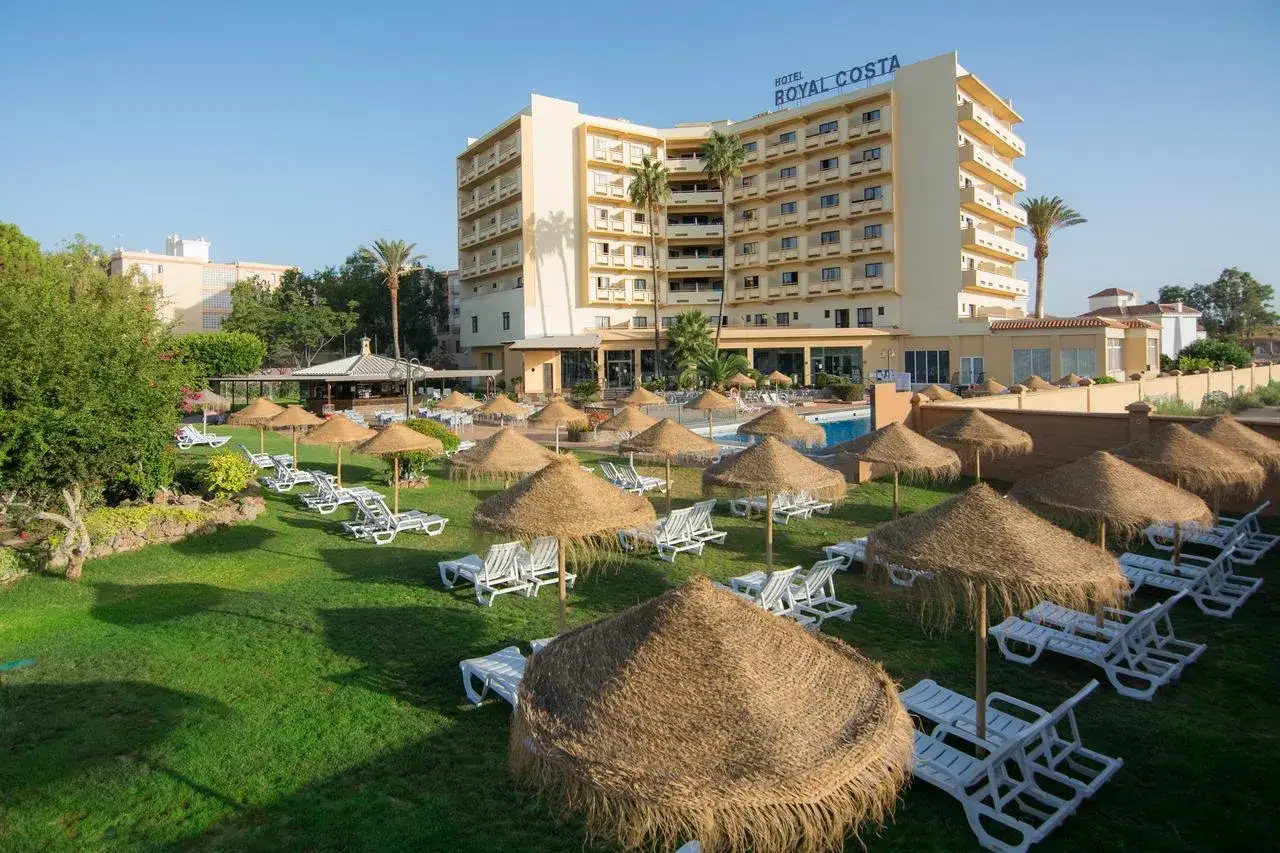 El hotel Royal Costa, con su piscina y tumbonas bajo sombrillas de paja, invita a relajarse en un día soleado.