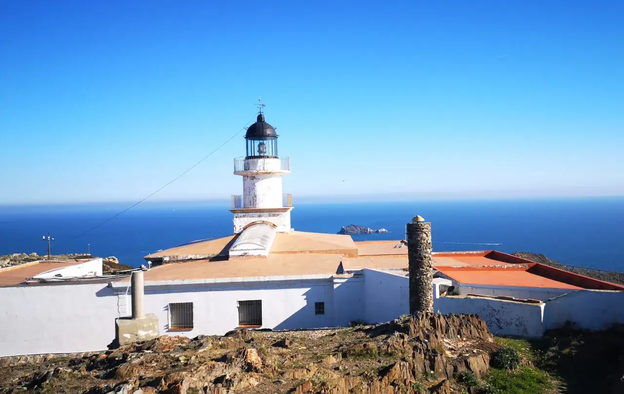 Faro blanco en Cap de Creus, con el mar azul intenso de fondo y un cielo despejado.
