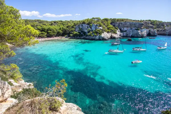 Calas turquesas y veleros, ideal para saber qué ver en Menorca en 3 días. Disfruta de playas paradisíacas y acantilados verdes.